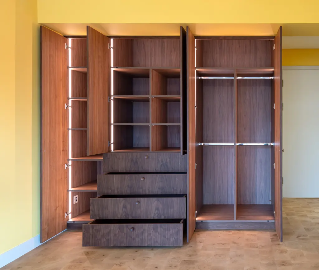 Open walnut wardrobe with lit shelving, hanging rails and drawers